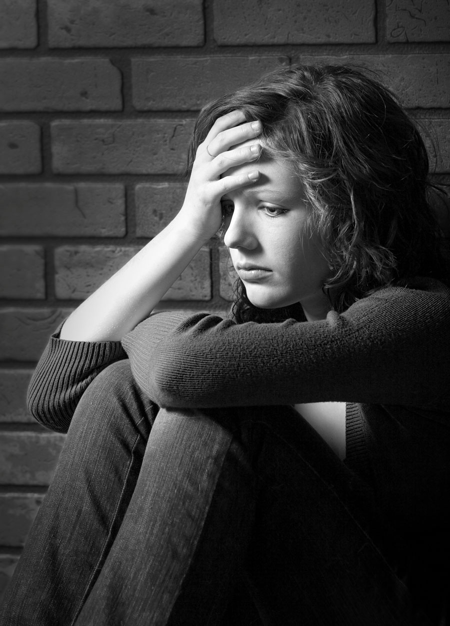 Teenage girl siiting against brick wall in a depressed state